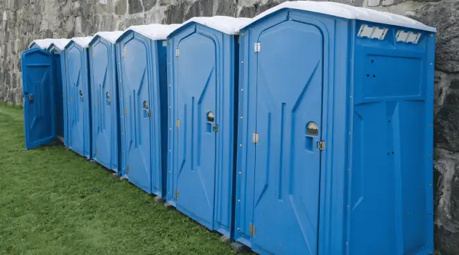 Row of blue portable toilets lined up on grass against a stone wall for event sanitation in Hollywood, FL