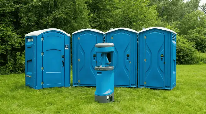 Four blue portable toilets and a matching hand washing station on grass near trees, a common sight at local outdoor events in Hollywood, FL